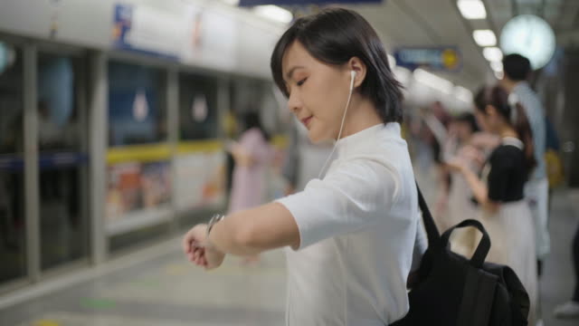 Portrait-of-asian-woman-with-earphone-listening-music-and-using-smartphone-for-chatting-with-friends-or-browsing-while-waiting-for-a-train.-Technology-in-everyday-life-and-travel.