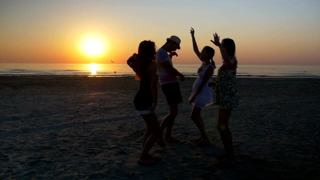 Männchen-mit-drei-Freundinnen-tanzen-am-Strand-bei-Sonnenuntergang