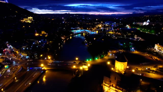 Beautiful-river-flowing-under-illuminated-city-bridges-after-dark,-aerial-shot