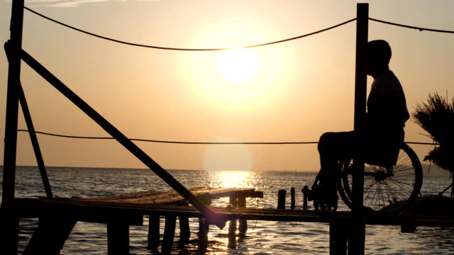 Silhouette-der-Mann-mit-schmerzenden-Füßen-auf-Rollstuhl-am-Pier-Meer-Sonnenuntergang-im-Sommer-Reisen