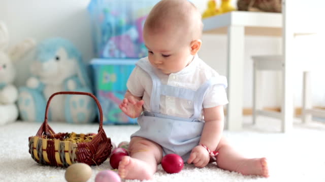 Cute-little-toddler-child,-baby-boy,-in-sunny-living-room-playing-with-Easter-chocolate-bunny-and-colorful-Easter-eggs