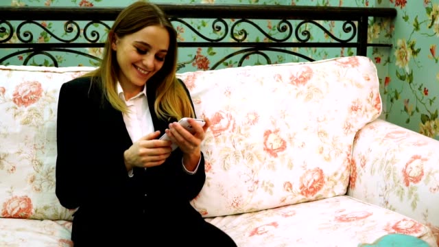 A-young-girl-in-a-suit-laughs-while-holding-a-smartphone-in-front-of-her,-looks-at-the-camera