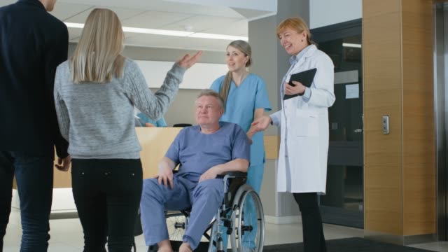 In-the-Hospital-Female-Doctor-Shows-Tablet-Computer-to-Elderly-Patient-in-the-Wheelchair.-Modern-Hospital-with-Best-Possible-Care.