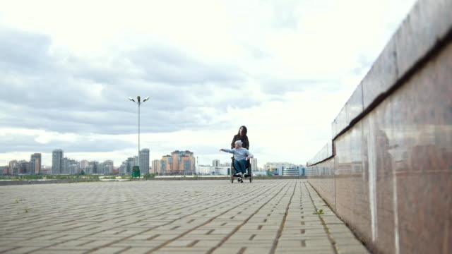 Behinderte-Menschen-im-Rollstuhl-mit-jungen-Frau-zu-Fuß-in-die-Stadt-Straße