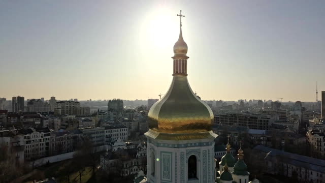 Ve-el-ojo-de-un-pájaro,-video-panorámico-desde-el-drone-en-FullHD-a-la-cúpula-dorada-de-la-campana-de-torre-de-Santa-Sofía-de-Catedral-en-la-ciudad-de-Kiev,-Ucrania-contra-un-sol-brillante.