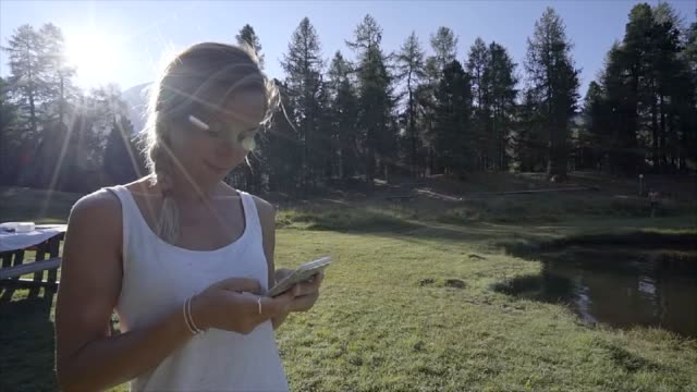 Junge-Frau-in-der-Natur-genießen-Sommer-Textnachrichten-auf-dem-Handy-bei-Sonnenuntergang;-Menschen-Jugend-Kultur-Technologie-Konzept