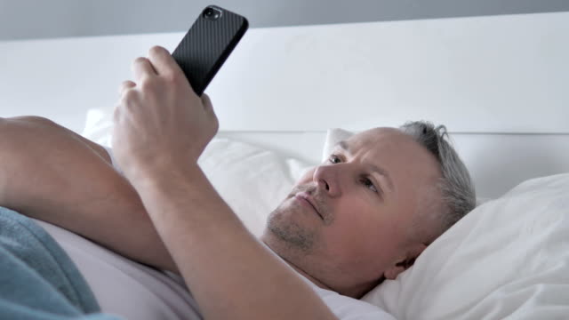 Gris-de-pelo-hombre-utilizando-Smartphone-mientras-que-mentir-en-la-cama