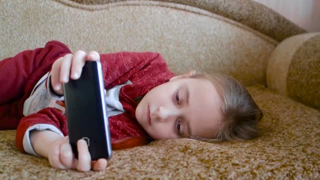 Chica-adolescente-viendo-un-video-en-el-teléfono-mientras-yacía-en-el-sofá.