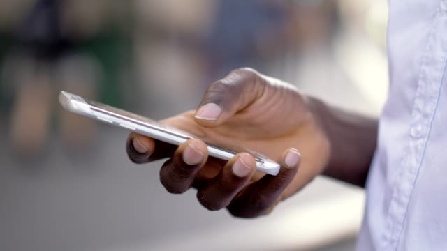 Nahaufnahmen-Porträt-des-jungen-afrikanischen-Man-es-Hands-Holding-Modern-Smartphone.-Schwarzer-Mann-tippen-am-Telefon-in-der-Innenstadt
