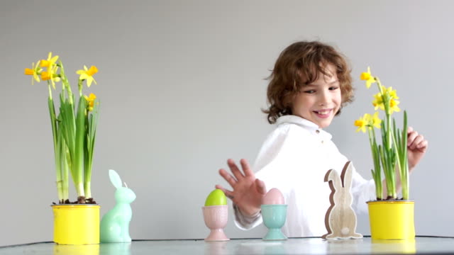 Boy-steals-an-Easter-egg,-childish-pranks.-Curly-cute-schoolboy-near-the-table-with-Easter-decor.-Easter-traditions