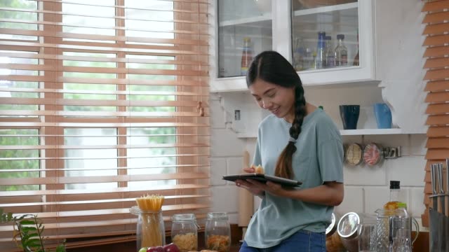 Junge-asiatische-Frau-mit-Tablette-und-Brot-essen.-Technik,-soziales-Netzwerk,-Kommunikationskonzept-in-der-Küche-zu-Hause.