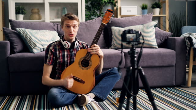Junge-Blogger-ist-Aufnahme-Tutorial-über-das-Spielen-von-Gitarre-für-Internet-Blog-mit-Kamera-zu-Hause