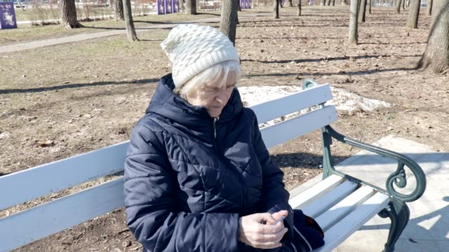 Una-anciana-anciana-sentada-en-un-banco-en-el-parque-al-aire-libre-y-usando-un-teléfono-inteligente-tocando-ella-está-usando-el-teléfono-inteligente-para-conectarse-con-personas-en-redes-sociales,-mensajes-de-texto-Ang-buscando-Internet