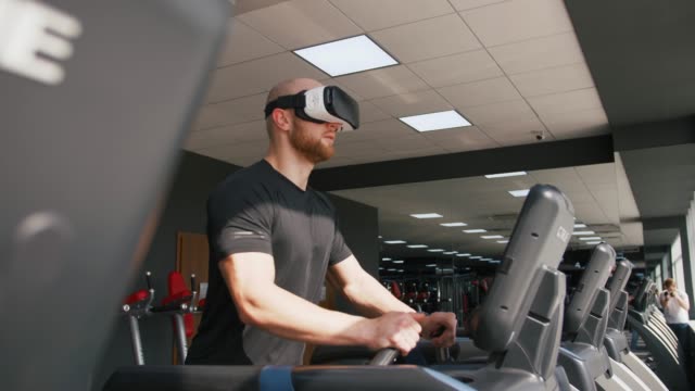 Joven-fuerte-haciendo-ejercicio-en-la-cinta-en-el-gimnasio,-usando-gafas-VR,-cámara-lenta