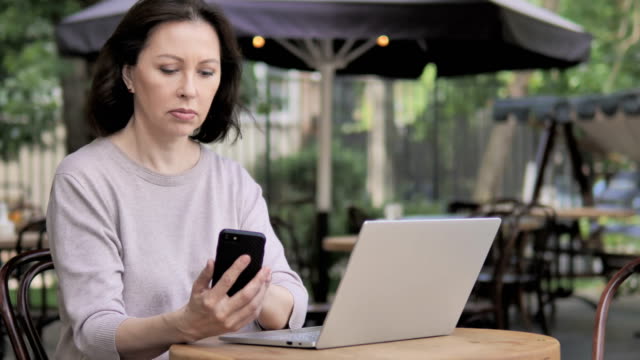 Alte-Frau-mit-Smartphone-und-Laptop,-Sitzen-im-Outdoor-Café
