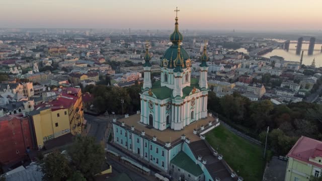 Flying-around-St.-Andrew's-Church-in-Podil-district-near-the-bank-of-Dnieper-in-Kyiv-(Kiev),-Ukraine-during-sunrise.-Aerial-shot,-4K