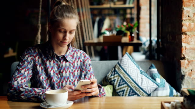 Attraktive-junge-Frau-mit-modernen-Smartphone-in-Café-berühren-Bildschirm