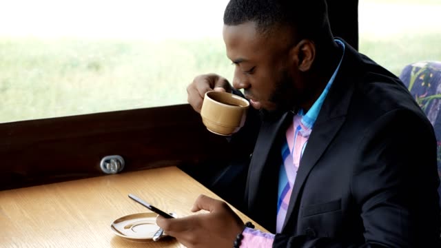 Afro-american-businessman-is-typing-a-message-on-smartphone-sitting-in-cafe.
