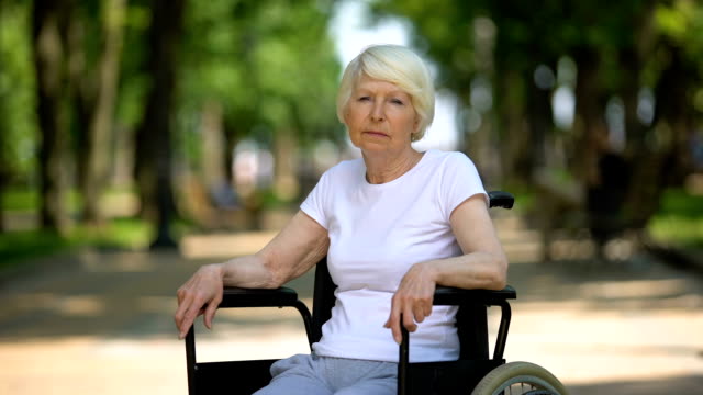 Frustrierte-Seniorin-im-Rollstuhl,-die-im-Krankenhauspark-vor-die-Kamera-schaut
