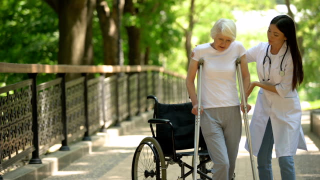 Doctor-helping-disabled-old-woman-walking-with-crutches,-recovery-after-trauma