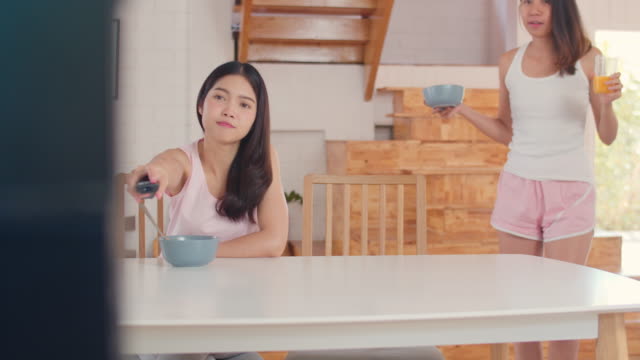 Asiatische-lesbische-Paar-fernsehen,-während-frühstücken-auf-dem-Tisch-in-der-Küche-in-morgendliche-San.
