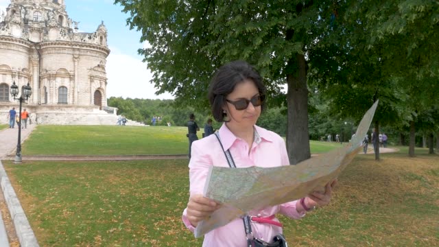 brunette-woman-looks-at-paper-map-against-the-background-of-a-historic-building