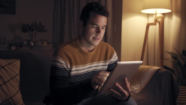 Porträt-eines-lächelnden-Mannes,-der-am-späten-Abend-auf-der-Couch-sitzt-und-mit-digitalem-Tablet-zu-Hause-arbeitet,-filmisch