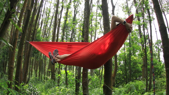 Mujer-relajándose-en-hamaca-con-teléfono-inteligente-en-la-selva-tropical,4k