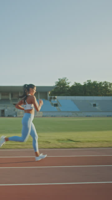 Beautiful-Fitness-Woman-in-Light-Blue-Athletic-Top-and-Leggings-is-Starting-a-Sprint-Run-in-an-Outdoor-Stadium.-Athlete-Doing-Her-Sports-Practice.-Slow-Motion.-Vertical-Screen-Orientation-Video-9:16