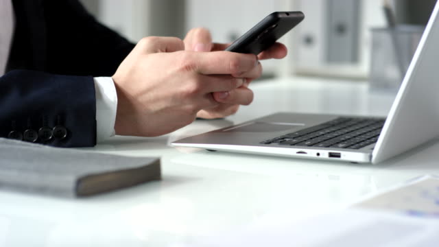 Hands-of-Businessman-Typing-Message-on-Smartphone-at-Office-Desk