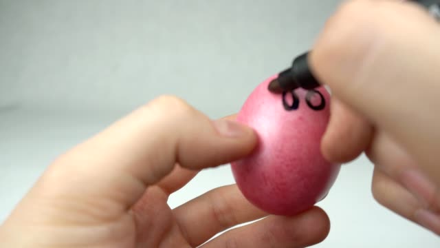 A-man-paints-with-a-felt-tip-pen-a-red-Easter-egg-draws-a-smiley-and-a-face,-a-holiday,-close-up