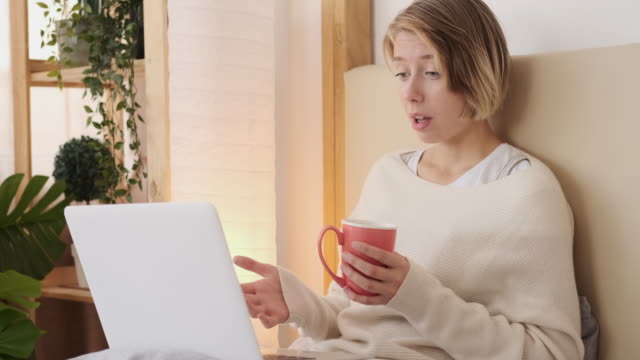 Frau-Video-anruft-mit-Laptop-sitzend-auf-dem-Bett