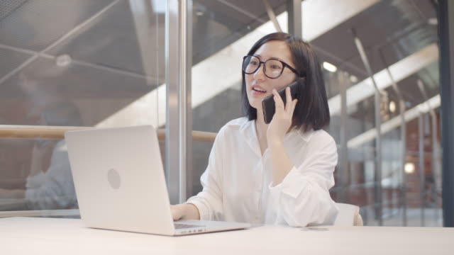 Hübsche-asiatische-Frau-mit-Telefonanruf-am-Arbeitsplatz