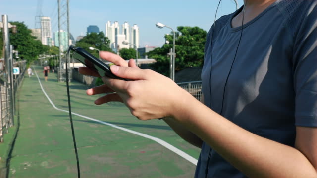 Asiatische-Sportlerinnen,-die-Smartphones-nutzen,-die-nach-dem-Laufen-die-Herzfrequenz-überprüfen.-Jogging-Workout-Lifestyle-auf-der-Straße-bei-Sonnenuntergang.-Gesunder-Lebensstil.