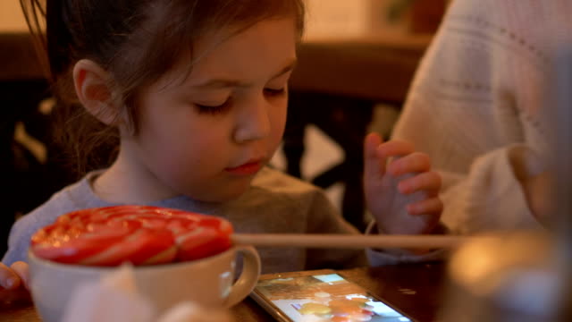 kleines-Kind-schaut-Video-auf-Smartphone-am-Tisch-im-Café