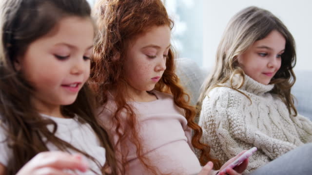 Gruppe-von-Mädchen-mit-Freunden-sitzen-auf-dem-Sofa-zu-Hause-spielen-auf-digitalen-Tablet-und-Handys