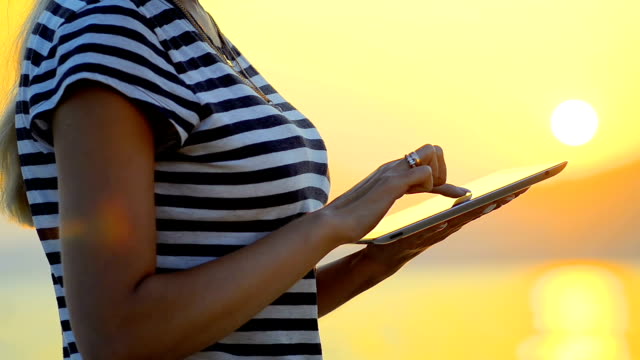 Close-up-a-girl-uses-a-tablet-by-the-sea-on-the-sunset.