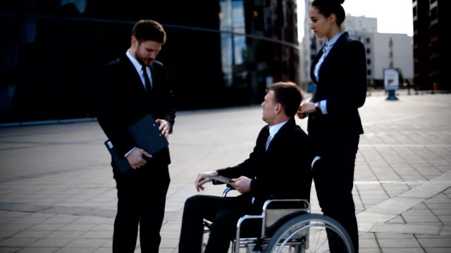 Young-disabled-entrepreneur-businessman-talk-with-his-coworkers-and-sign-textpad-docs