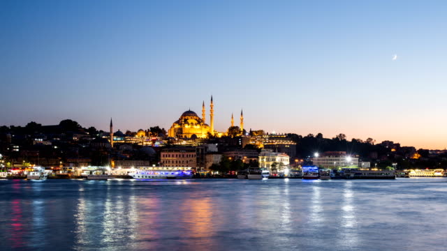 Zoom-out-Timelapse-view-of-Istanbul-cityscape-with-Suleymaniye-mosque-with-tourist-ships-floating-at-Bosphorus-at-night