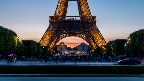 Eiffelturm-Tag-zu-Nacht-Zeitraffer-und-Menschen-sitzen-auf-dem-Rasen-am-Abend-in-Paris,-Frankreich