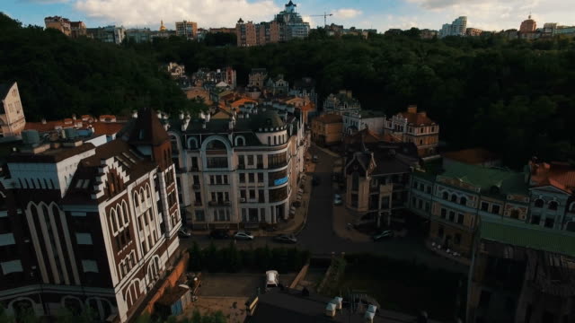 Drohne-Kamera-bewegt-sich-unter-den-Dächern-von-Gebäuden-auf-die-alten-europäischen-Gassen-mit-bunten-Häusern-und-Fußgänger-bei-Sonnenuntergang-4K