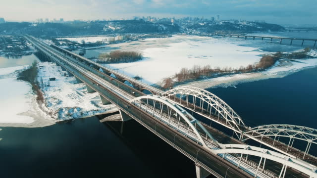 Auto-und-Zug-bewegt-sich-auf-einer-Brücke-über-einen-gefrorenen-Fluss-Luftbild-Drohne-Filmmaterial