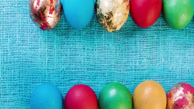 Huevos-de-Pascua-multicolores-hermosa-están-dispuestos-en-dos-filas-horizontales-en-una-lila-de-tela,-mantel-azul.-Fondo-de-celebración-para-la-semana-Santa.-Espacio-para-texto.-Closeup-de-huevos-de-Pascua.