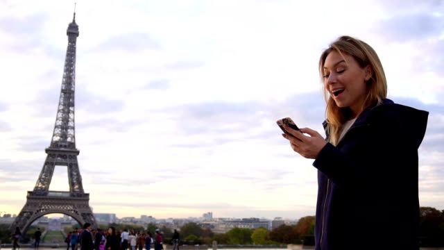 Fröhliche-Frau,-die-im-Chat-per-Smartphone-mit-Eiffelturm-Hintergrund
