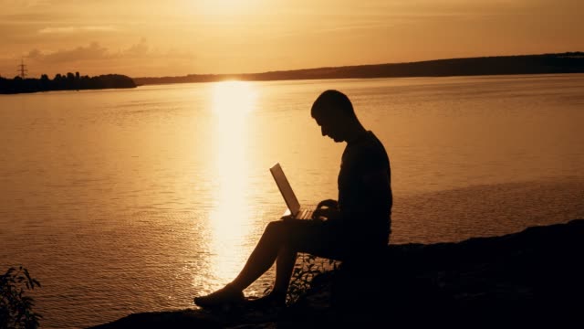 Mann-sitzen-und-arbeiten-auf-dem-Laptop-von-Sonnenuntergang-Hintergrund-auf-dem-Hügel