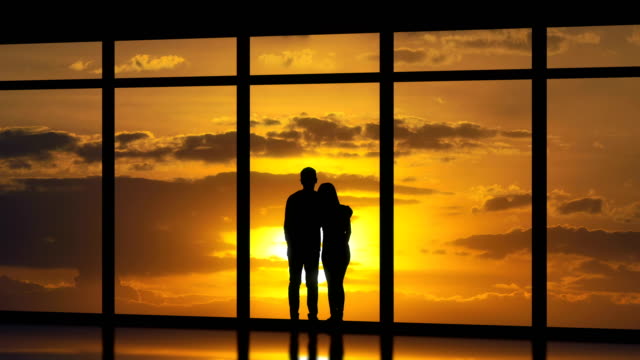 The-couple-standing-near-windows-on-the-sunset-background.-time-lapse