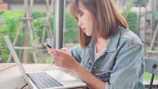 Geschäftskunden-freie-asiatische-Frau-arbeiten,-Projekte-auf-Laptop-und-Smartphone-beim-Sitzen-am-Tisch-im-Café.-Lebensstil-smart-schöne-Frauen-arbeiten-bei-Coffee-Shop-Konzepte.