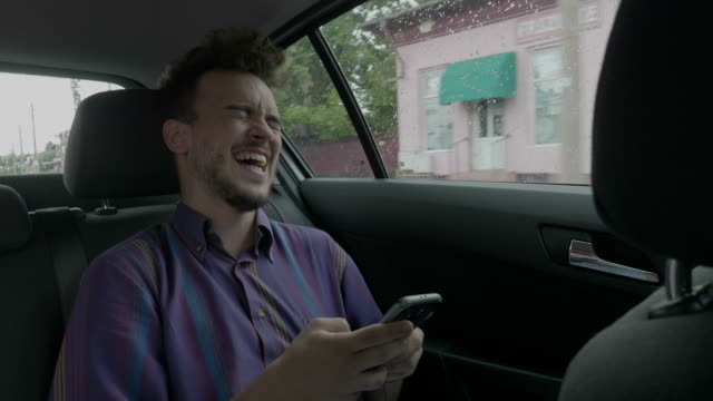 Hipster-Jüngling-Passagier-im-Chat-und-SMS-auf-Touchscreen-mit-seinem-Smartphone-laughing-out-loud,-an-etwas-lustiges-in-der-Uber-Taxi-Auto