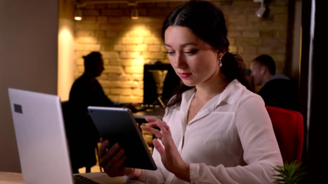 Closeup-portrait-of-young-caucasian-female-office-worker-browsing-on-the-tablet-in-front-of-the-tablet-on-the-workplace