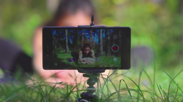 Young-brunette-woman-vlogger-shooting-workout-process-video-for-her-blog-in-a-park-with-smartphone